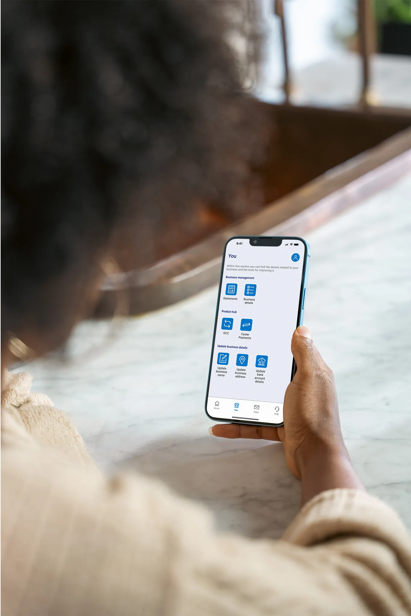 Person holding a smartphone displaying a business payments app while seated at a marble table