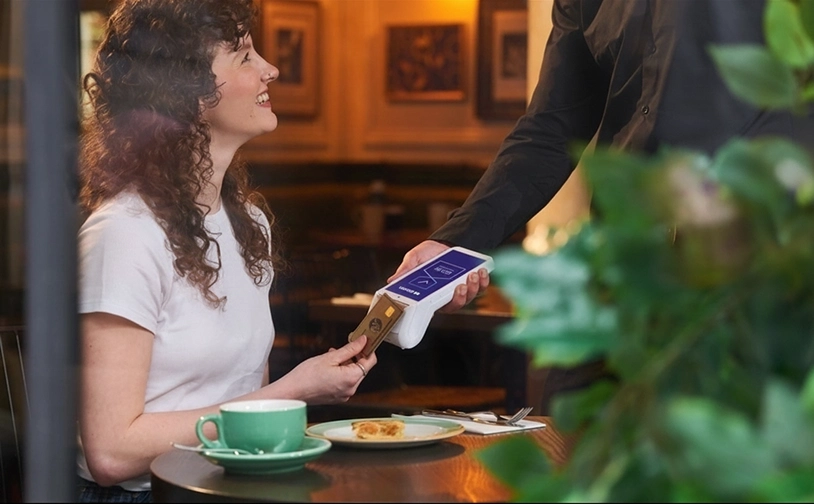 Contactless card payment at a bar using a handheld POS terminal while bartender serves cocktails