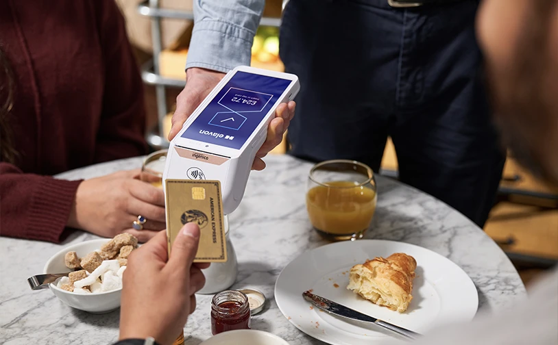 Customer making a face‑to‑face card payment at a café table using a handheld card payment terminal