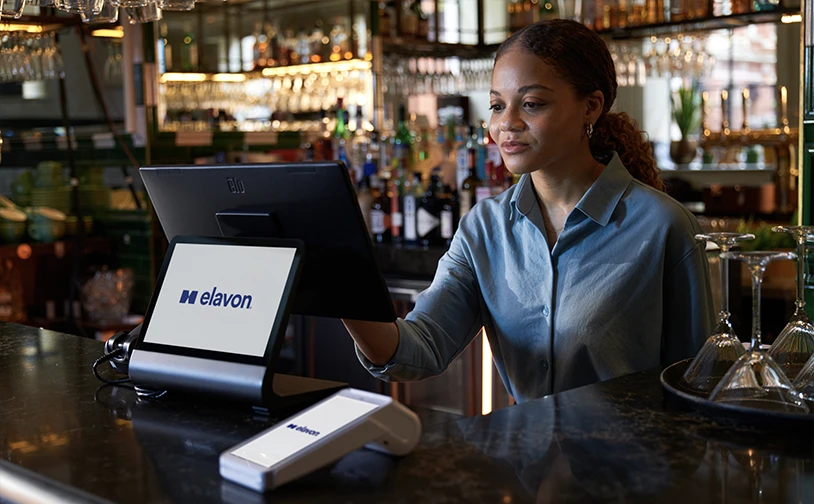 Bar staff using an Elavon point‑of‑sale system and card payment terminal at a modern bar counter