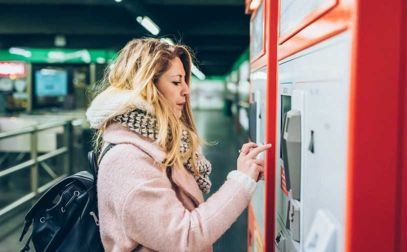 A person holds a smartphone against a contactless payment reader on public transport to tap in