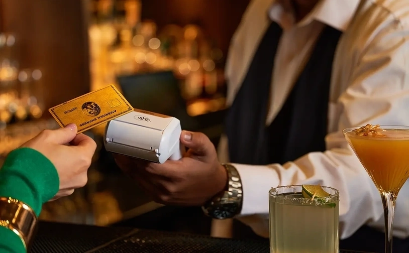 Contactless card payment being processed on a portable card reader in a bar with drinks on the counter