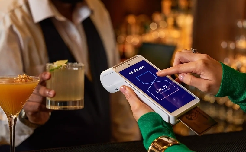Customer using a handheld card payment device showing transaction amount while holding a card at a bar