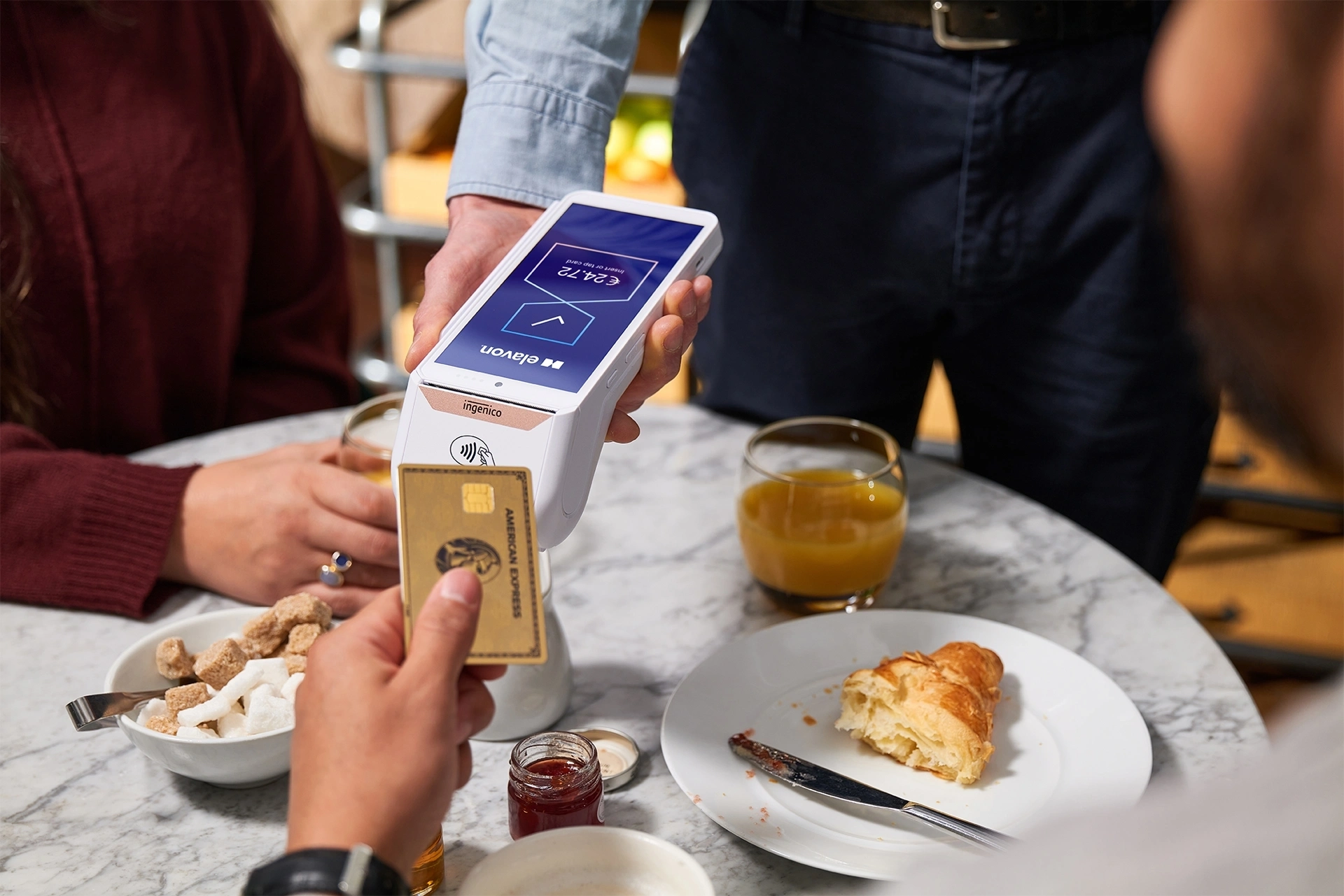 Customer making a face‑to‑face card payment at a café table using a handheld card payment terminal