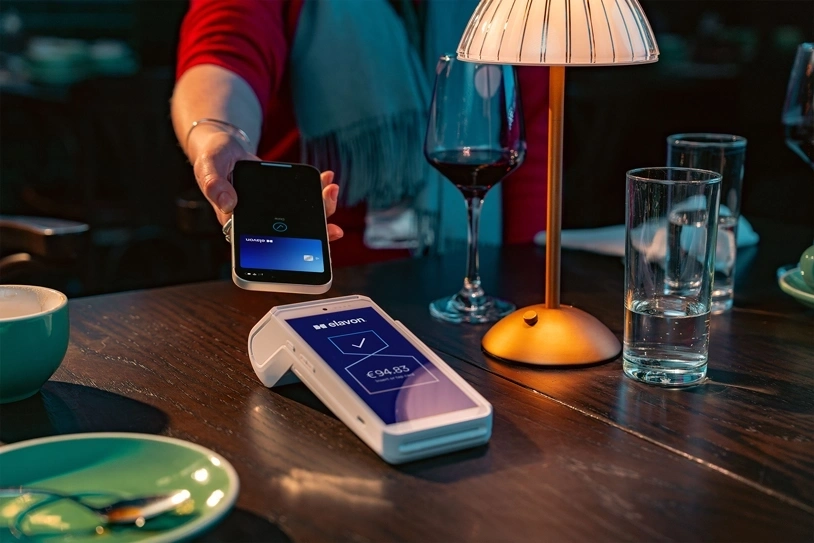 Customer making a mobile contactless payment at a restaurant table using a card payment terminal