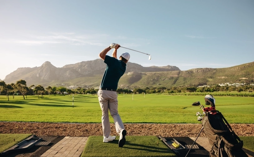 Golfer swinging on a sunny driving range with mountain backdrop